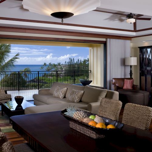 A luxurious living room with wicker furniture, a dining table, and an open view of the ocean through large sliding glass doors.