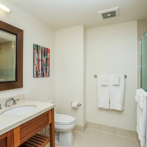 The image shows a bathroom with a sink, mirror, toilet, shower, and towels on the wall in a neat and modern design.