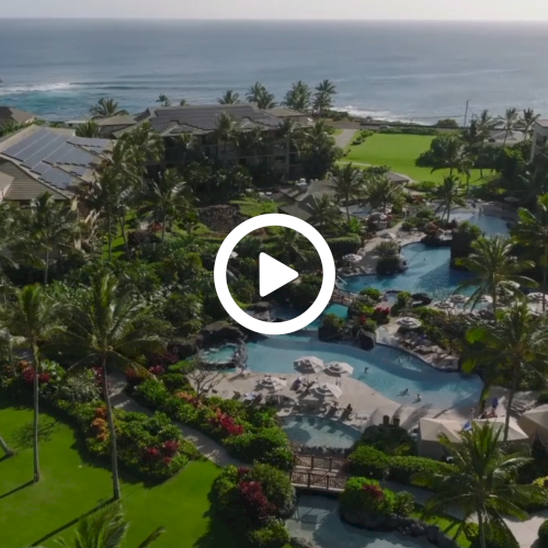 Aerial view of a luxurious resort featuring pools, palm trees, and buildings amid lush greenery by the ocean.