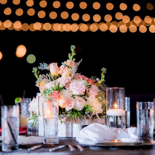 A beautifully set table with a floral centerpiece, surrounded by glasses and candles, under soft bokeh string lights.