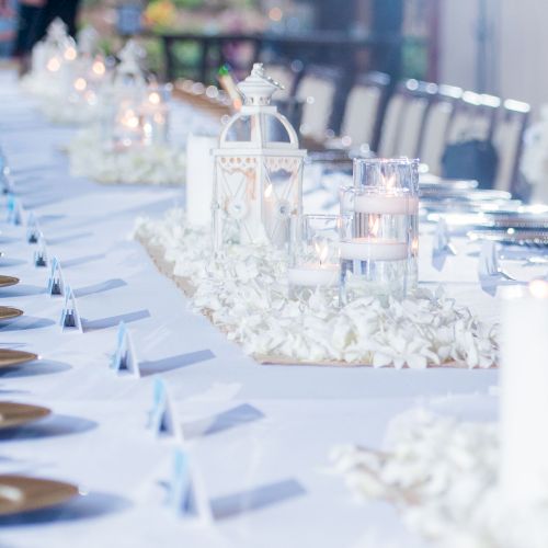 A long, elegantly set table features white decor, candles, and gold plates, ready for an event or celebration.